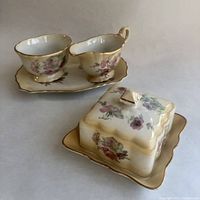 Butter dish, cream, sugar, and tray set arranged on flat surface showing floral and gold trim detail.
