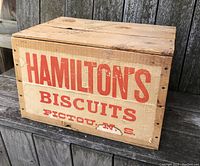 Front angled view of vintage wooden crate with nailed edges and red printed text reading Hamilton's Biscuits, Pictou N.S.