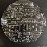Top-down view of round glass cheese platter showing embossed cheese names and central smooth surface with small white flaw.