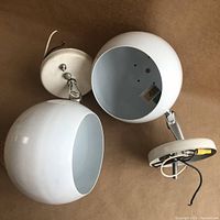Pair of white enamel spherical metal wall lamp shades with chrome adjustable arms and wiring visible, shown from top.