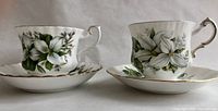 Photo showing both tea cups and saucers side by side, highlighting the trillium pattern and gold trim with scalloped edges.