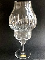 Clear cut crystal bulbous hurricane lamp shade with alternating short and tall vertical cuts on a black background.