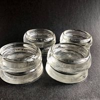 Four of the clear glass coasters shown stacked against a dark background highlighting their thick glass construction and rounded edges.