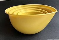 Side view of four nested yellow-orange teardrop-shaped mixing bowls showing size progression and shape including spouts and rims.