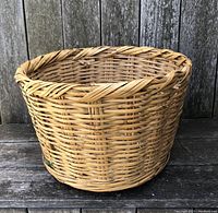 Side view of vintage wicker bushel basket showing woven pattern and braided top rim.