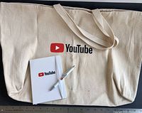 Full set showing cotton tote bag, mini notebook, and ballpoint pen with YouTube logo, placed on a flat surface with ruler showing tote bag size.