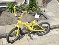 Full left side view of the yellow Adams MEGA Force bike on paved ground near stone wall and garden area, showing frame, tires, chain guard, seat, and handlebars.
