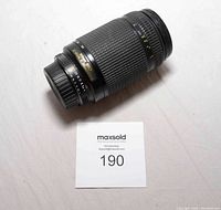 Full view of Nikon 70-300mm AF NIKKOR camera lens placed on white surface with maxsold number card.