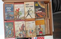 photo showing a box filled with various vintage paperback books including titles by Jules Verne, L. Frank Baum, and other classics