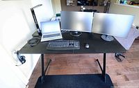 Front view of gaming desk with two computer monitors, laptop, keyboard, mouse on large black mouse pad. Cup holder attached on right side, headphone hook on left.