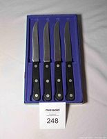 Set of four Henckels steak knives in blue velvet-lined box, arranged side by side showing full knives and handles