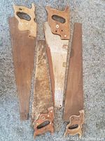 Four large hand saws laid out on floor showing wooden handles and varying blade conditions.