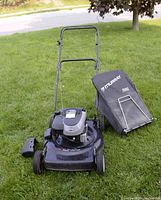 Front-left perspective showing mower deck, engine, side chute and grass bag