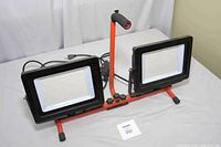 Full view of the dual LED work lights mounted on an adjustable orange/red metal frame with black casings and numerous small LED bulbs.