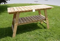 Front view of wooden work table with slatted top and bottom shelf on grass background.
