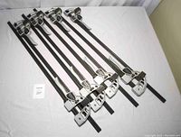 Eight 24-inch bar clamps with adjustable lever tension lying on a white surface, showing full length and handles.