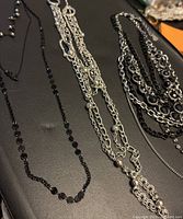 Top-down photo of three multi-tier extended chain necklaces displayed on a black surface.