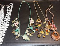 Four unique necklaces laid out flat on a dark surface showing varied styles including beads, charms, and a large heart pendant.