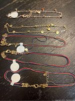Five ankle bracelets laid out on a dark surface, showing chain styles and bead colors
