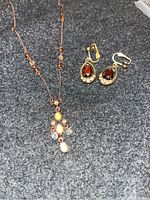Photo shows a pair of antique clip earrings with dark red stones and clear crystals, and a matching necklace with a decorative multi-stone pendant on a thin chain.