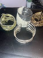 Five expandable band bracelets displayed on a black surface: 3 beaded bands (yellow-green, white-black, gold-black), one twisted silver-tone band, one gold-tone beaded band.