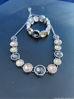 Clear image of a necklace and a coil bracelet laid on a dark surface featuring round citrine and obsidian stones in silver-tone settings.