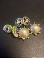 Photo showing three pairs of clip-on earrings on black background including floral porcelain, faux pearl, and silver-tone metal filigree styles.