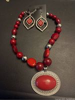 View of the red beaded necklace and matching earrings on a black background.