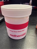 White plastic jar labeled 'Snow Face Mask 602' by Esthemax on a black surface