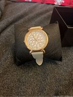 Front view of the ladies watch showing white strap, gold-tone case, and white dial with geometric star pattern and numbers around the edge.