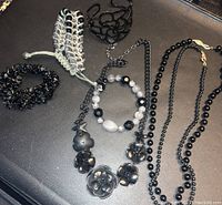 Photo showing seven black jewelry pieces including bracelets, necklaces, and a choker with various beads and flower motifs.