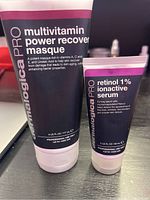 Photo shows two Dermalogica professional skincare products: Multivitamin Power Recovery Masque and Retinol 1% Ionavtive Serum tubes on a black surface.
