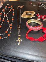 Full view of six jewelry items lying flat on a black surface including necklaces and bracelets of various colors and materials.