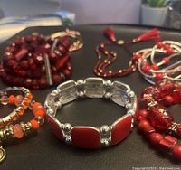 Photo showing multiple stretch bracelets in red and orange bead designs with silver-tone accents arranged on black surface.