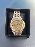 Front view of a new men's gold tone watch with crystal accents on bezel and strap, showing chronograph dial with Roman numerals.