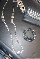 Photo showing long beaded necklace, wide bracelet, stretchy bracelet, and black studded wallet on black surface.
