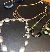 Photo showing silver-tone linked chain necklace and colorful glass bead necklaces with earrings on black surface