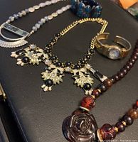 Various necklaces, watch, and bracelet on black surface for detailed viewing.