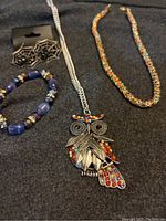 Photo of all four jewelry pieces: owl pendant necklace, gem chain, bracelet, and spiderweb earrings on black fabric background