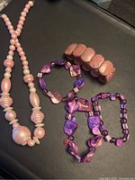Photo showing pink beaded necklace and four purple and pink beaded bracelets arranged on a black surface.