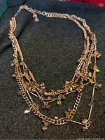 Multi-layer rosegold necklace with various charms including hearts, stars, and crystals laid on a dark fabric background.