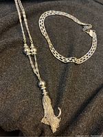 Full view of the two necklaces on black fabric background showing the tassel detail and bead clusters on one and linked CZ stones on the other.