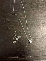 Three-piece sterling silver and cubic zirconia jewelry set laid on dark wooden surface. Includes necklace, earrings, and ring.