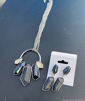 Clear view of silver-tone pendant necklace and matching earrings on white backing card