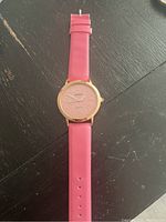Full view of the pink leather strap wristwatch with gold-tone case, placed on a dark surface