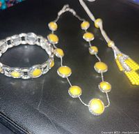 Photo showing silver-tone bracelet and portion of necklace with yellow circular accents on black background.