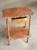 Full view of the antique wood side table showing top surface, central drawer with pull, and lower shelf with carved floral design.