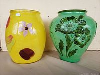 Photo showing both vases side by side: a yellow painted glass vase with flower motifs and a green ceramic pot with embossed flower designs