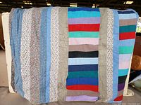 Quilt spread out showing multiple colored fabric stripes, floral patterns, and signs of wear such as loose threads and light soiling.