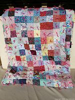 Full view of large handmade patchwork quilt with multicolored squares and red tassels.